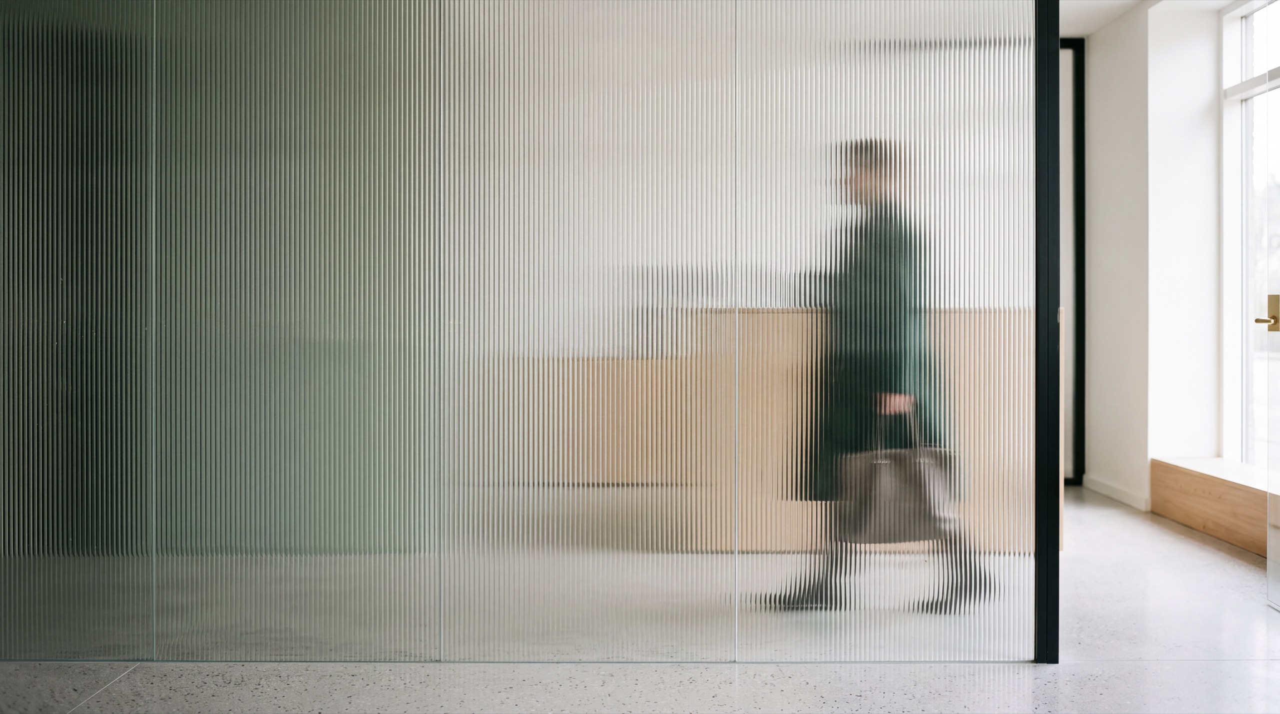 A figure passing behind a fluted glass partition in a Copenhagen law office.