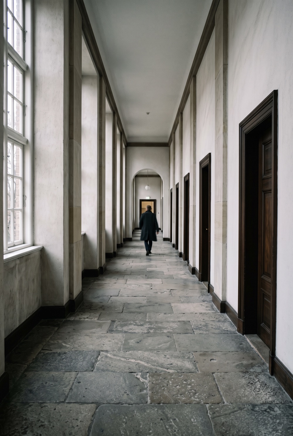 An empty courthouse corridor, a single figure walking away down the hall.